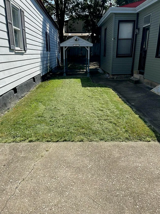 Side yard lawn and concrete walkway leading to a covered gate at the rear
